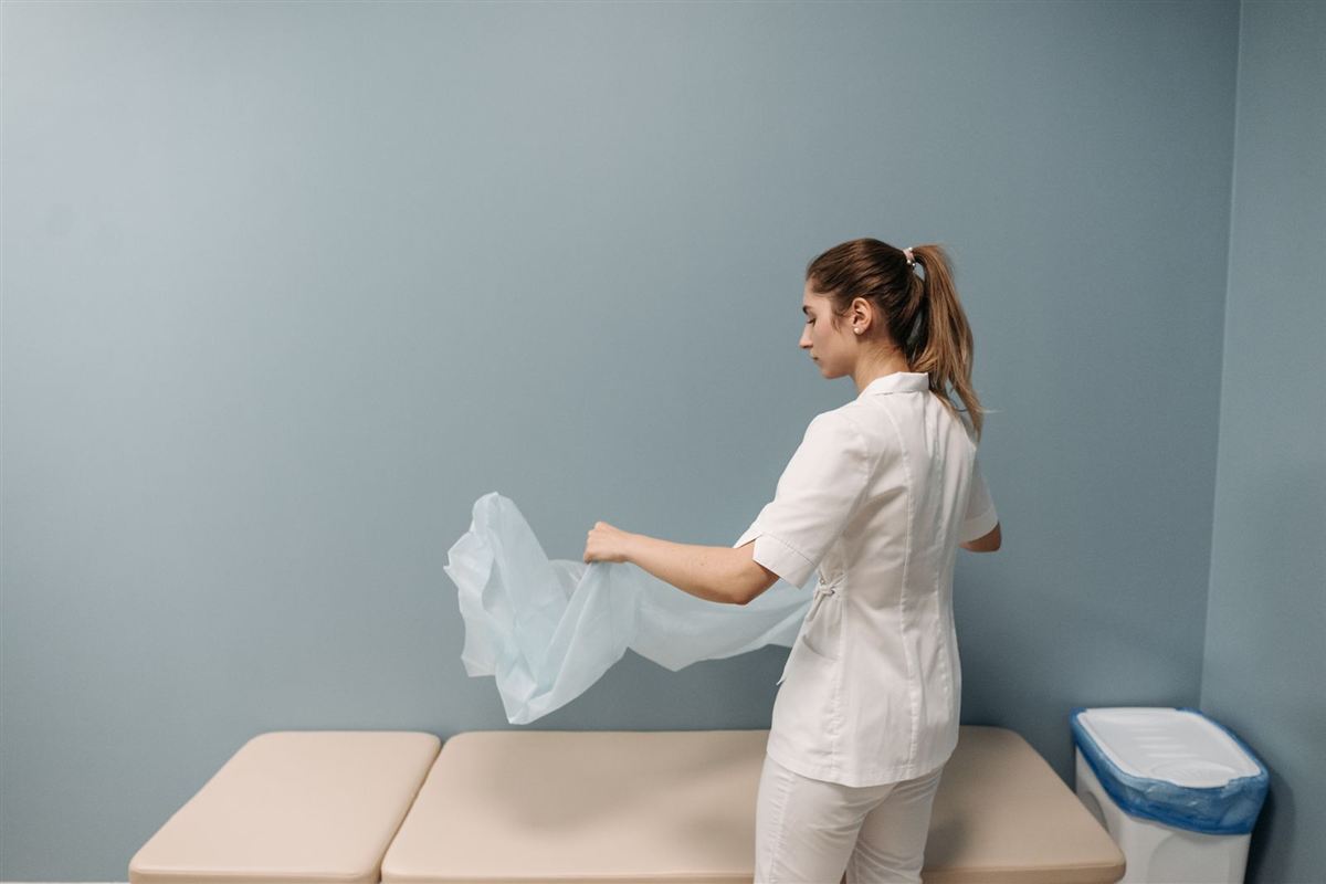 A staff member laying a fresh cover on an exam table in a medical office