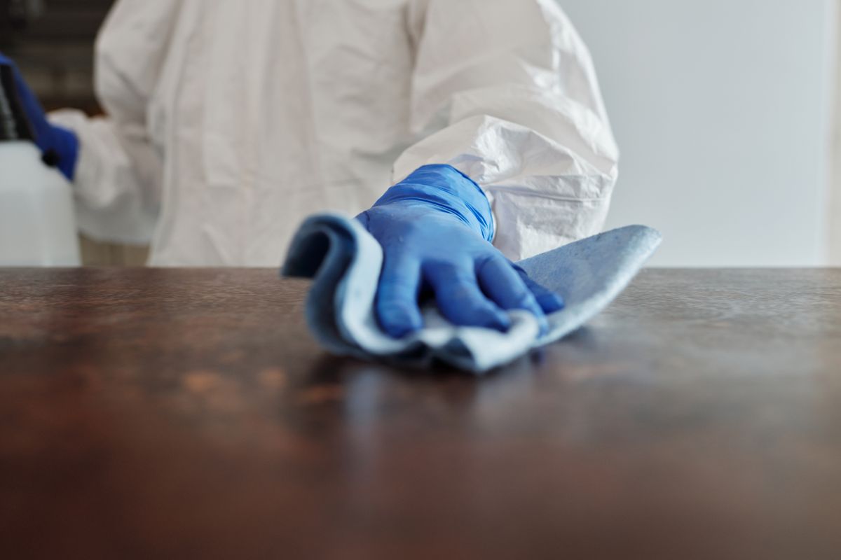 A gloved hand wiping a dark tabletop with a blue cloth