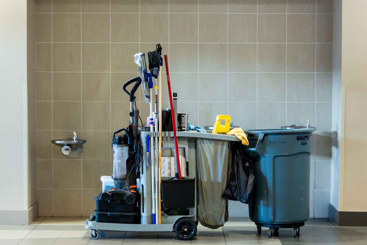 A stocked janitorial cart standing in a tiled corridor