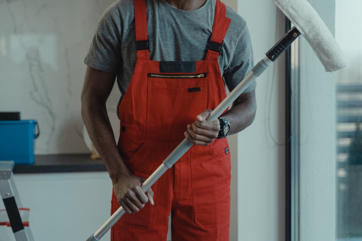 A cleaner in red overalls holding a window squeegee pole
