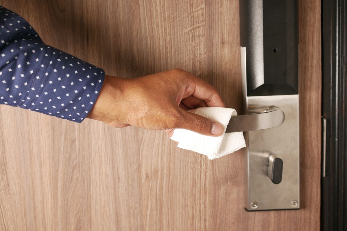 A hand wiping a metal door handle with a white cloth