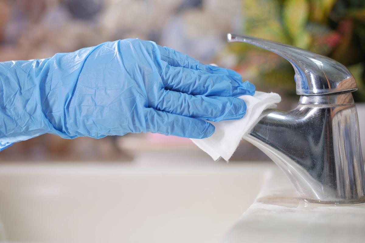 A gloved hand wiping a restroom faucet