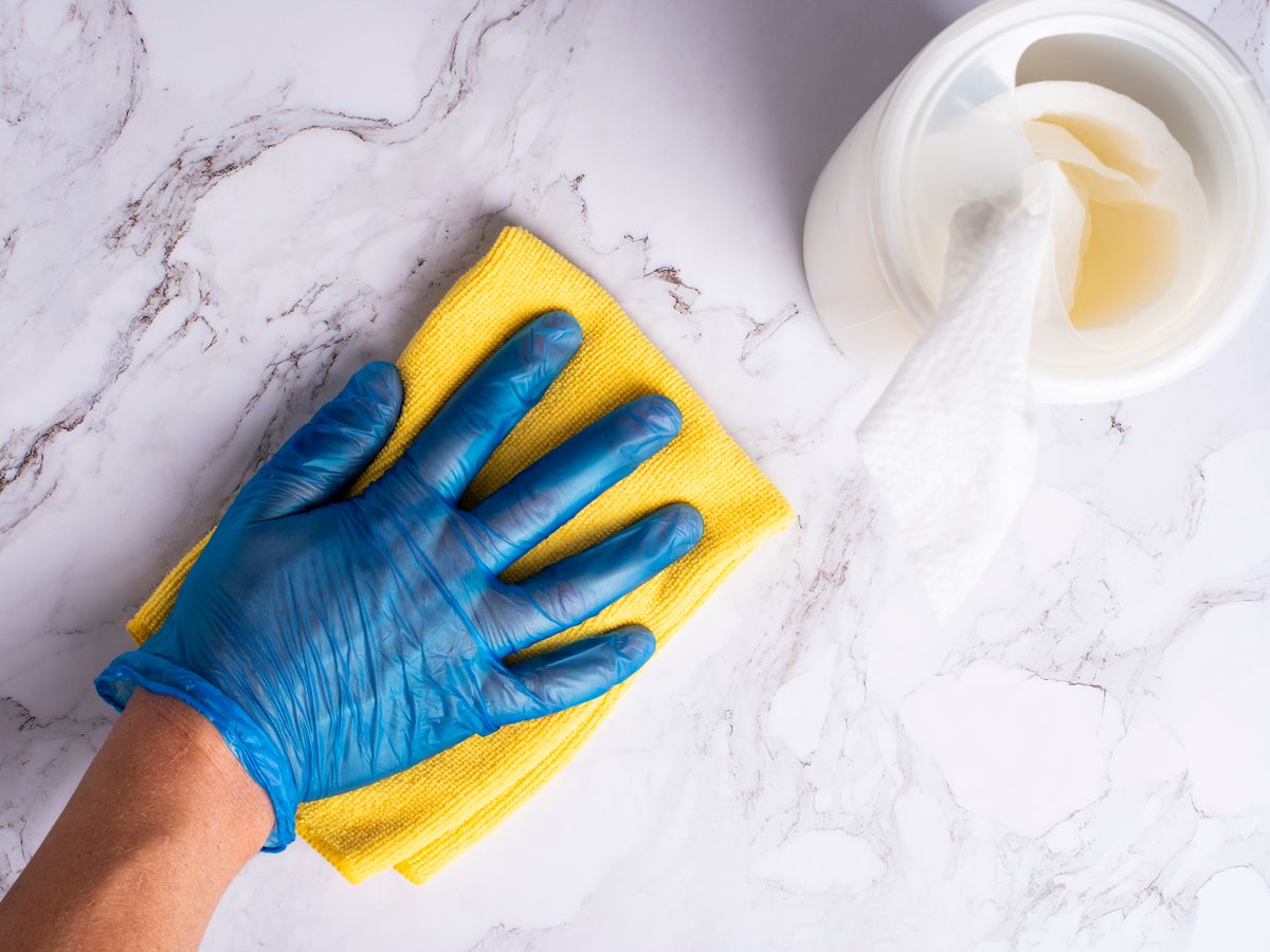 Gloved hand wiping a countertop with disinfectant and a cloth