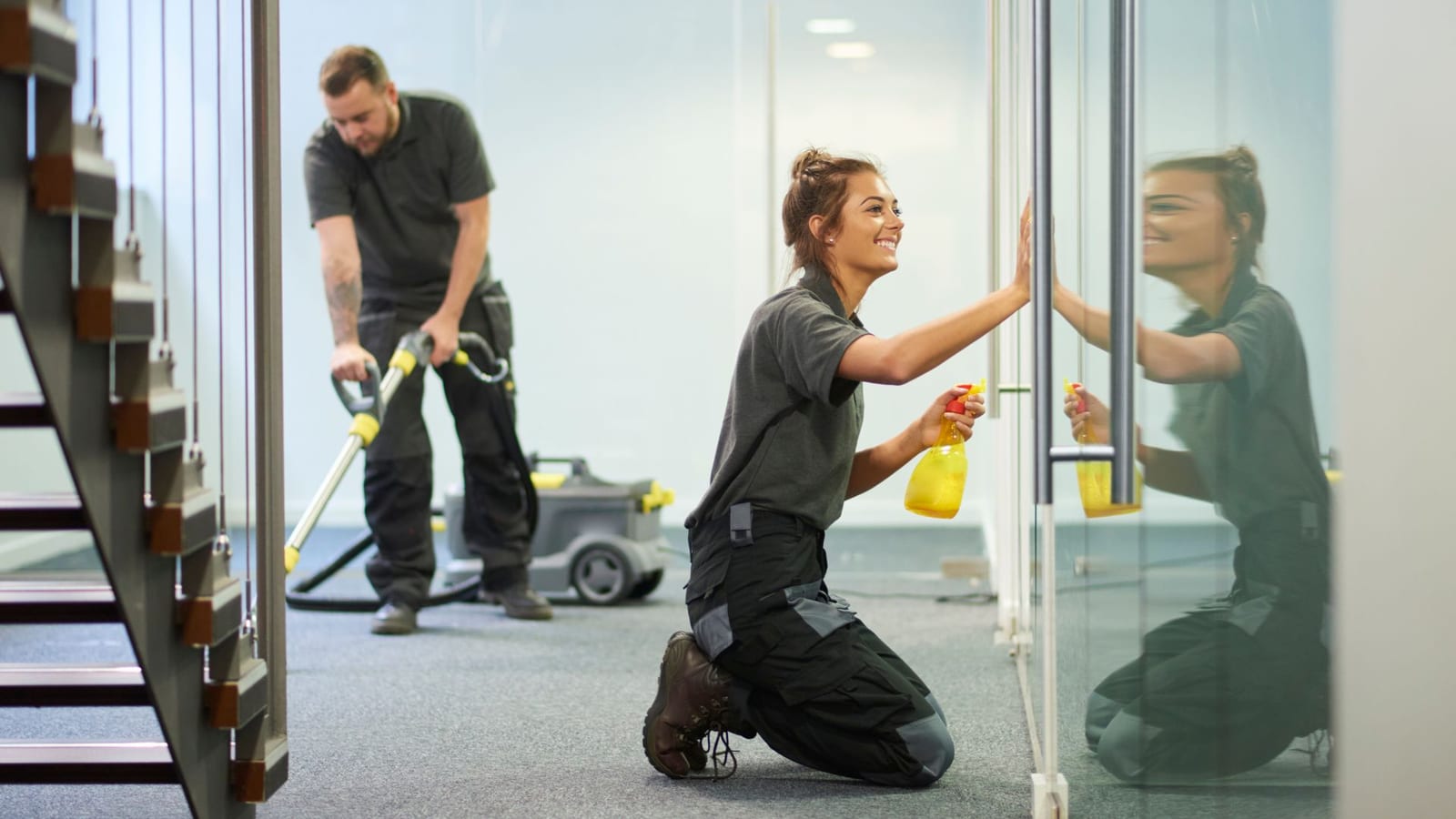 Cleaners wiping a glass partition and vacuuming an office: office cleaning services in Germantown, MD